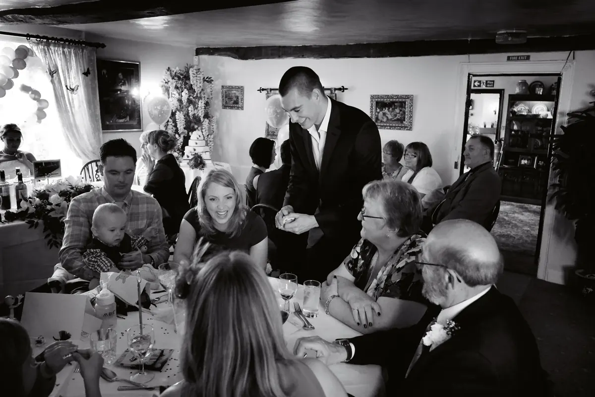 Black and white photo of Matt Parro performing magic for wedding guests seated in a reception room