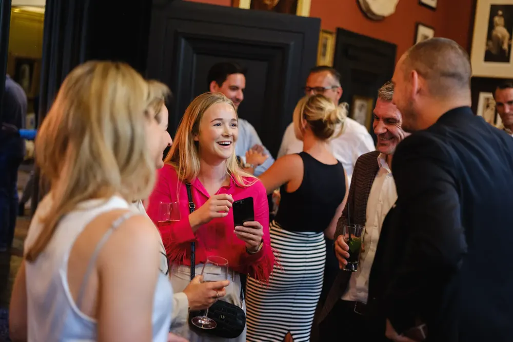 Guests laughing at Matt Parrou2019s phone magic at a drinks reception