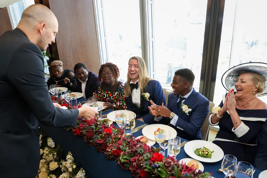 Matt Parro performing magic at the top table at a wedding as guests laugh and applaud