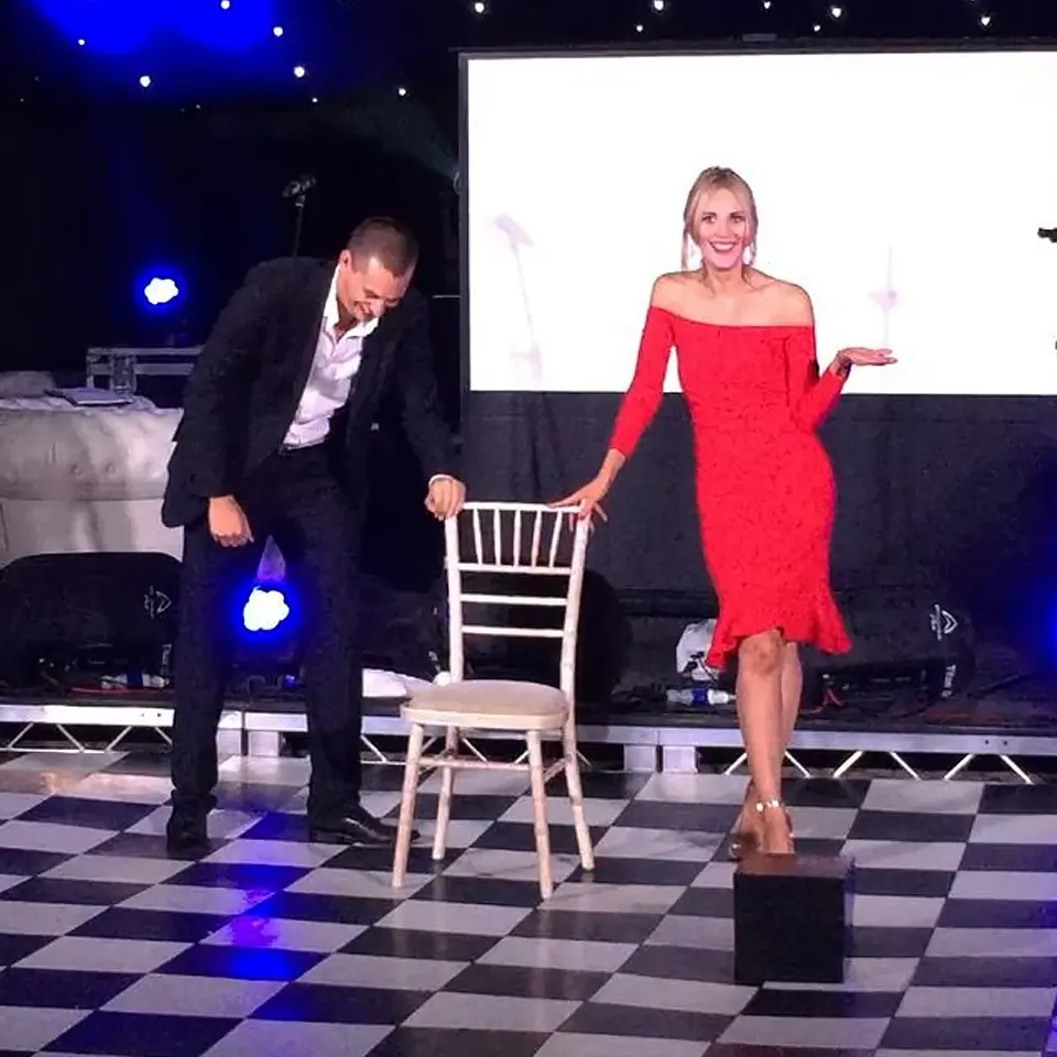 Stage magician Matt Parro performing with a volunteer on stage at a gala